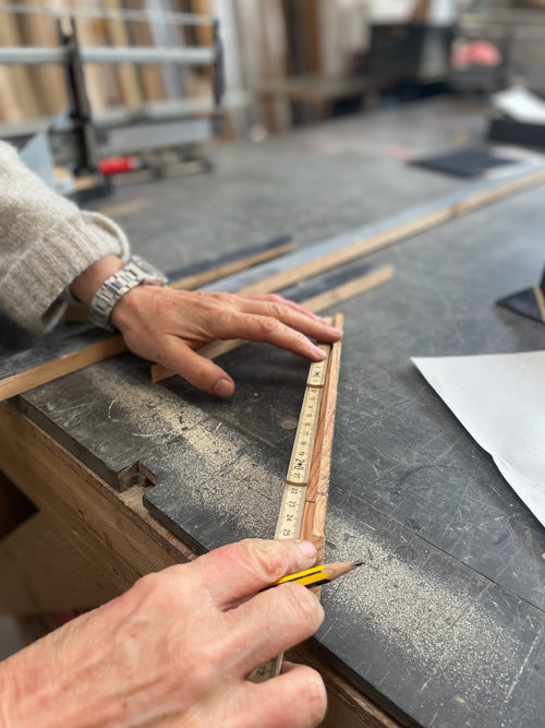 Nahaufnahme von Handwerkerhänden, die eine Bilderrahmenleiste mit Lineal und Bleistift im Frameworks Berlin Rahmenatelier abmessen.