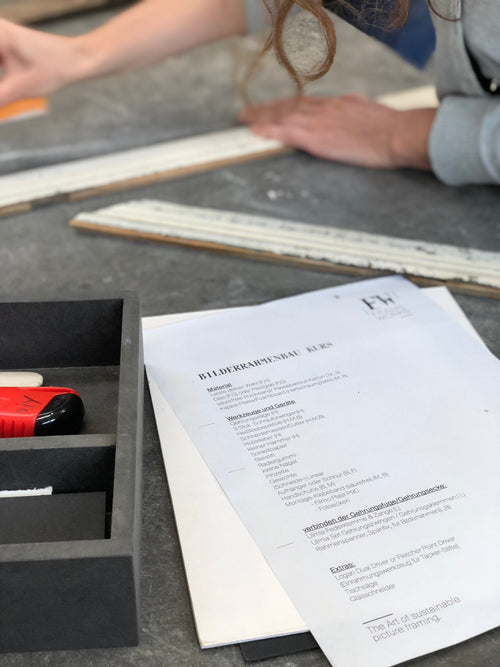Nahaufnahme von Rahmenbau-Kursunterlagen und Werkzeugen auf dem Arbeitstisch in der Frameworks Berlin Werkstatt.